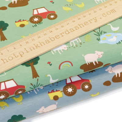 Fun, children's storybook farmyard print with tractors, pigs, sheep, chickens and trees on jersey fabric by John Louden in blue and green