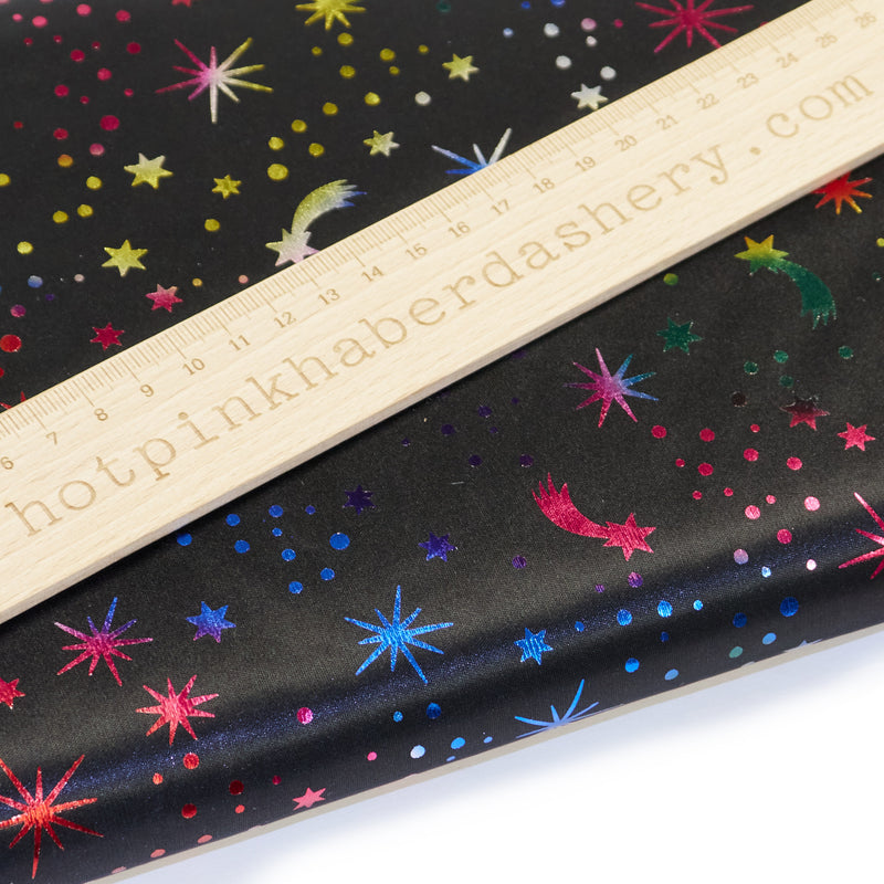 Fun, shimmery rainbow foil print with fireworks and shooting stars night sky multi colour fabric